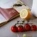 Flat lay of cooking ingredients including tomatoes and a lemon with a cookbook.