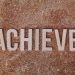 Wooden letters spelling 'ACHIEVE' on a textured brown surface, conveying motivation and success.